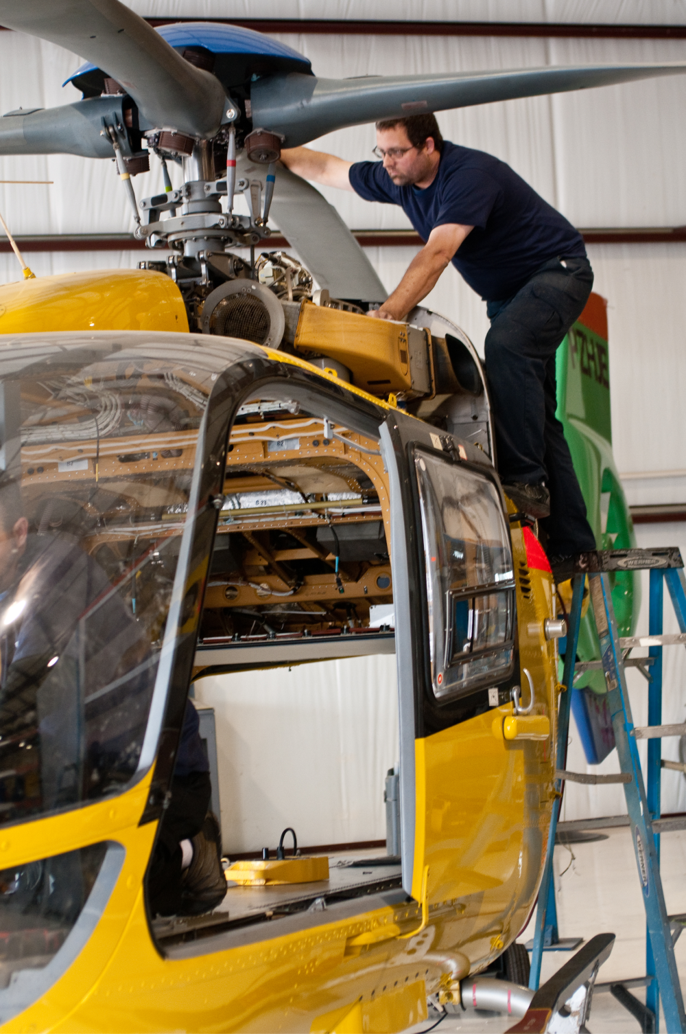 Crew member repairing helicopter rotor. 