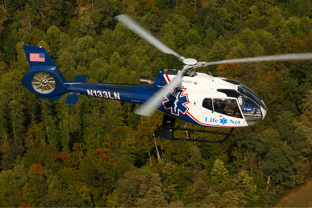 Air Methods helicopter flying over forest.